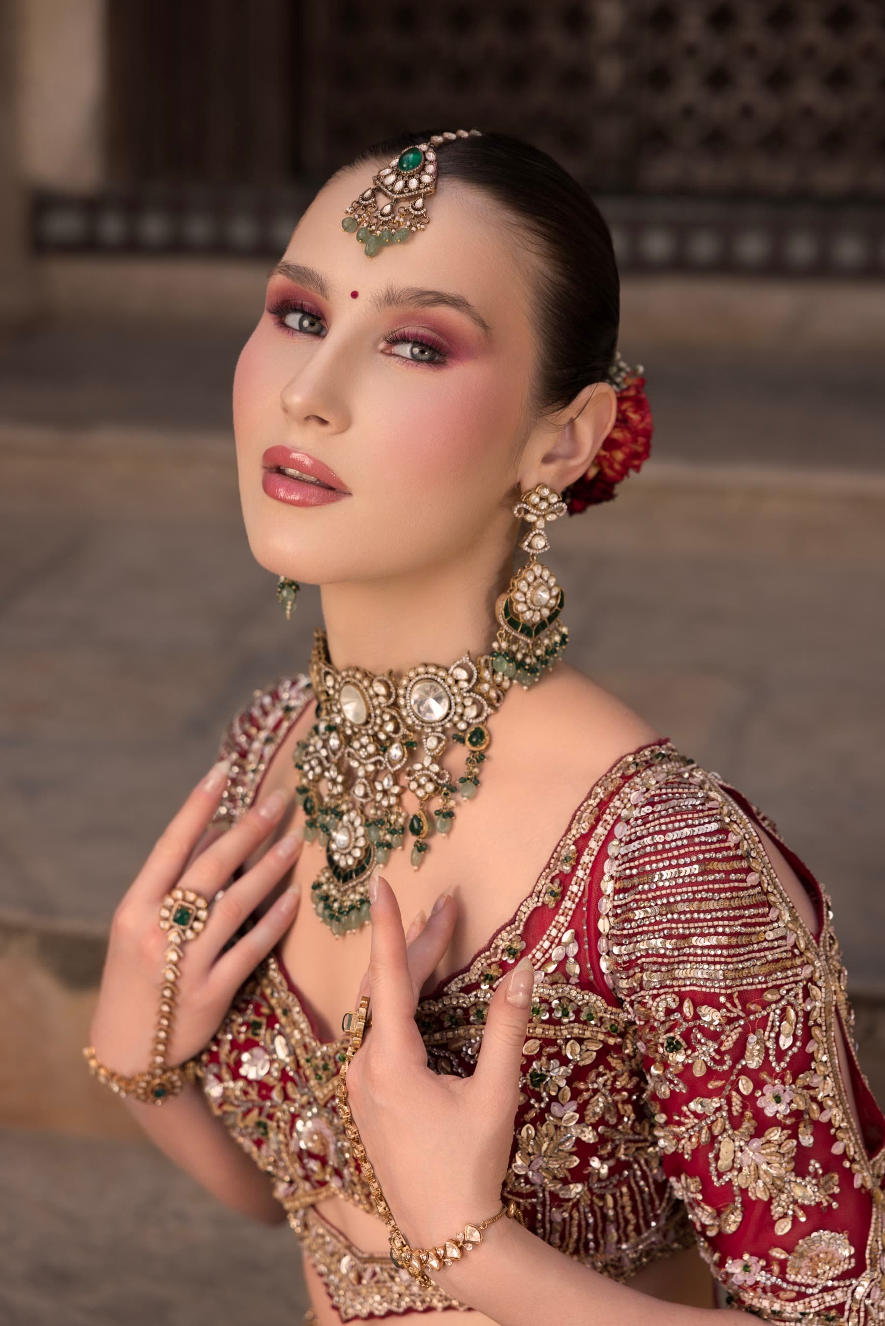 A bride in red, hands raised, kundan choker at the throat