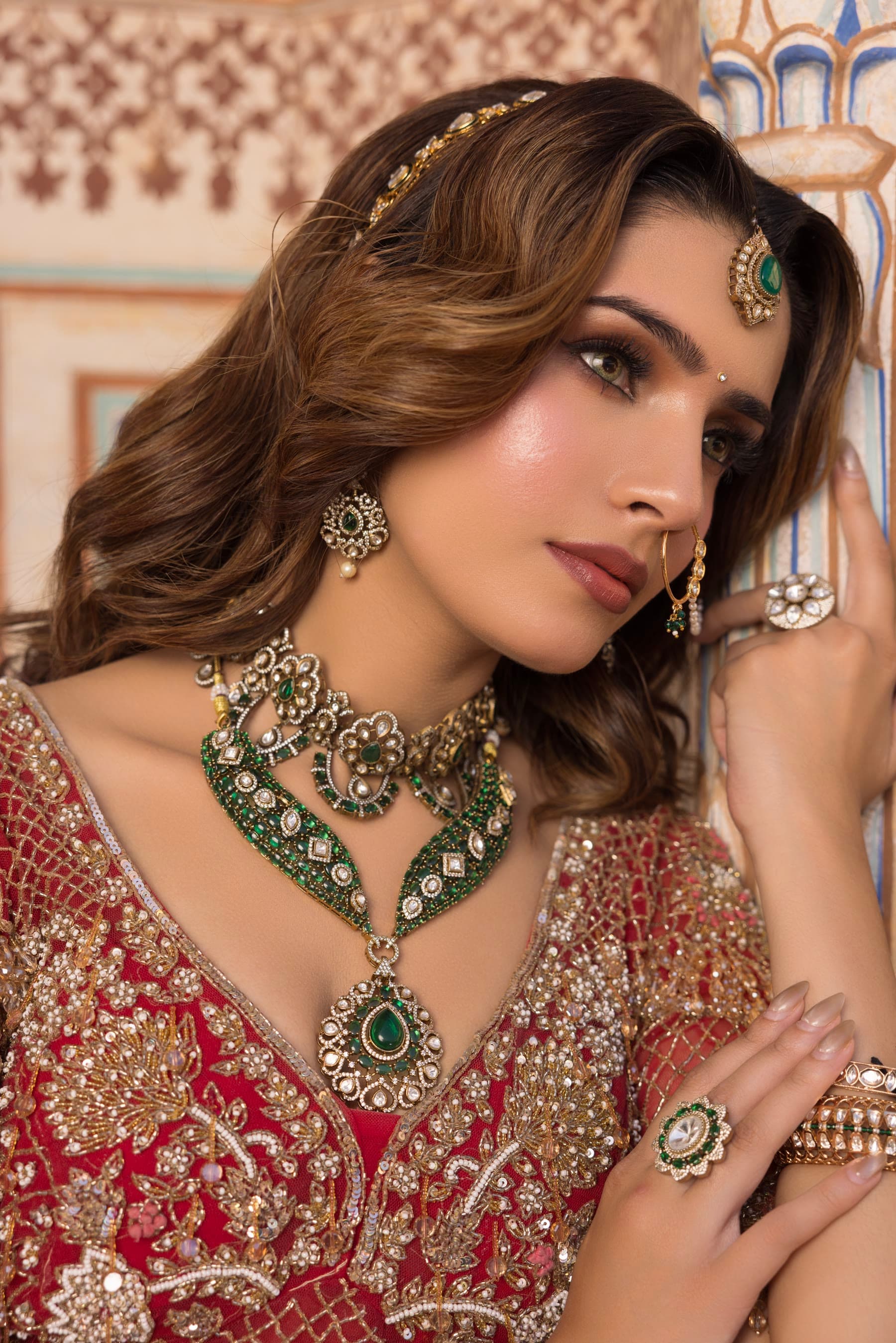 A bride lifting one hand towards her face, emerald at the throat