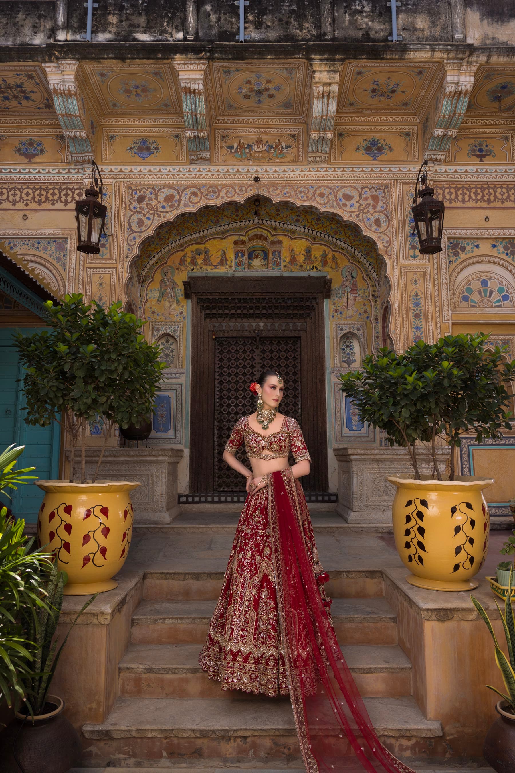 A bride on the steps of a painted haveli, veil trailing down
