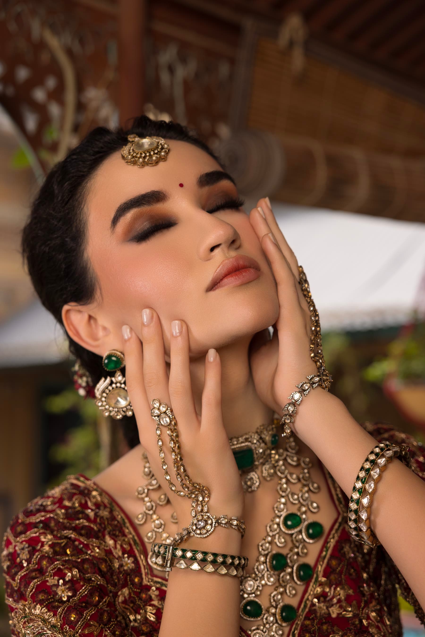 Both hands framing the face, kundan and emerald across the fingers