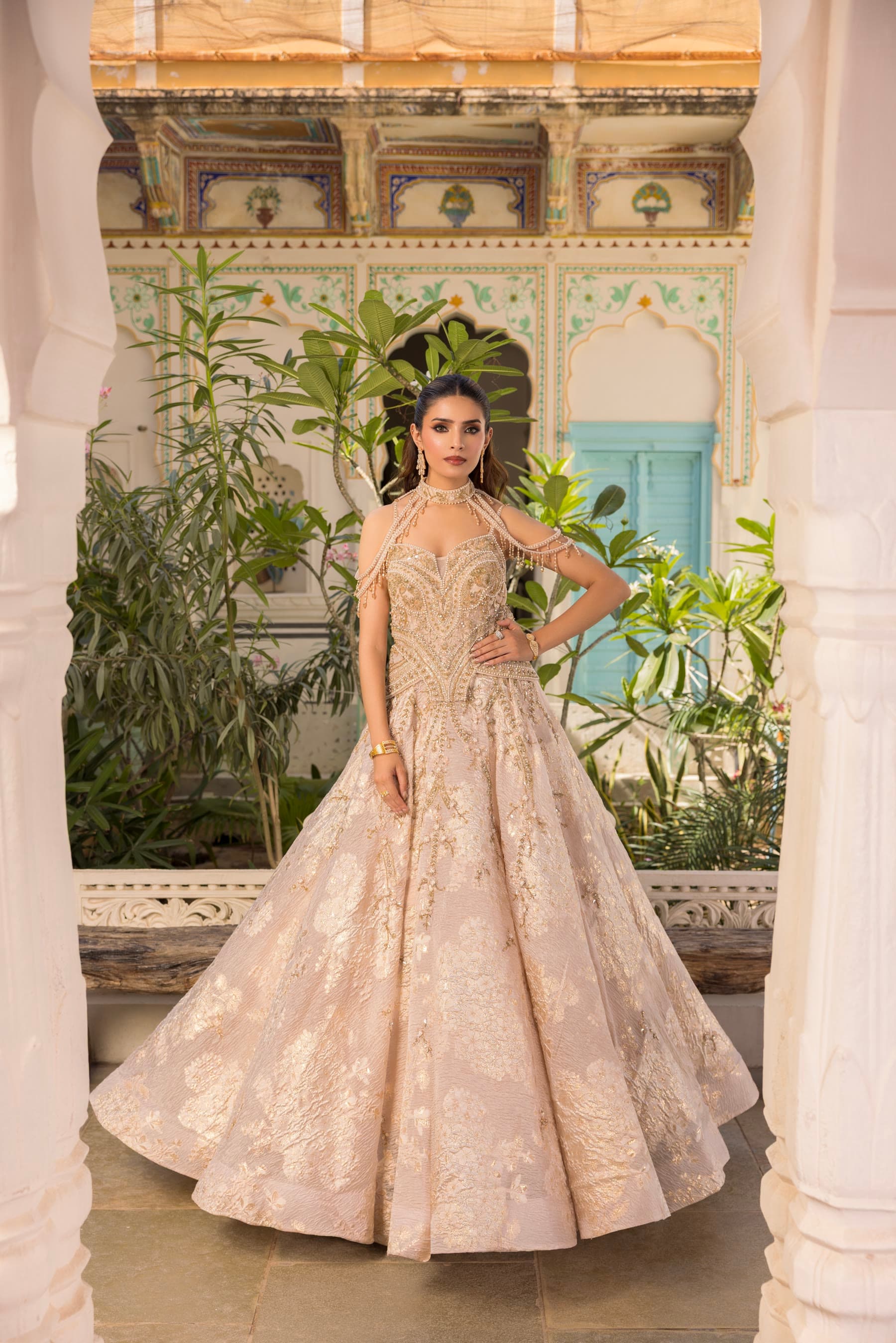 A pale courtyard, the bride full length under turquoise shutters