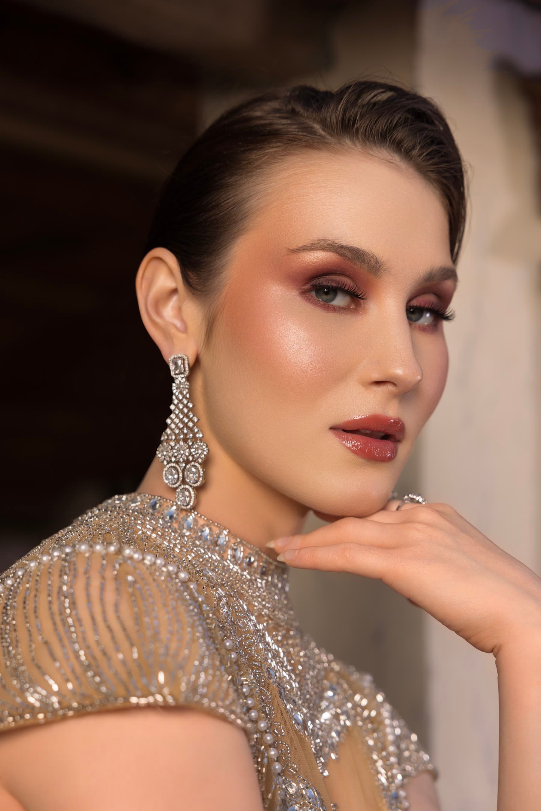 Editorial close: bronze lid, slicked hair, hand at the jaw