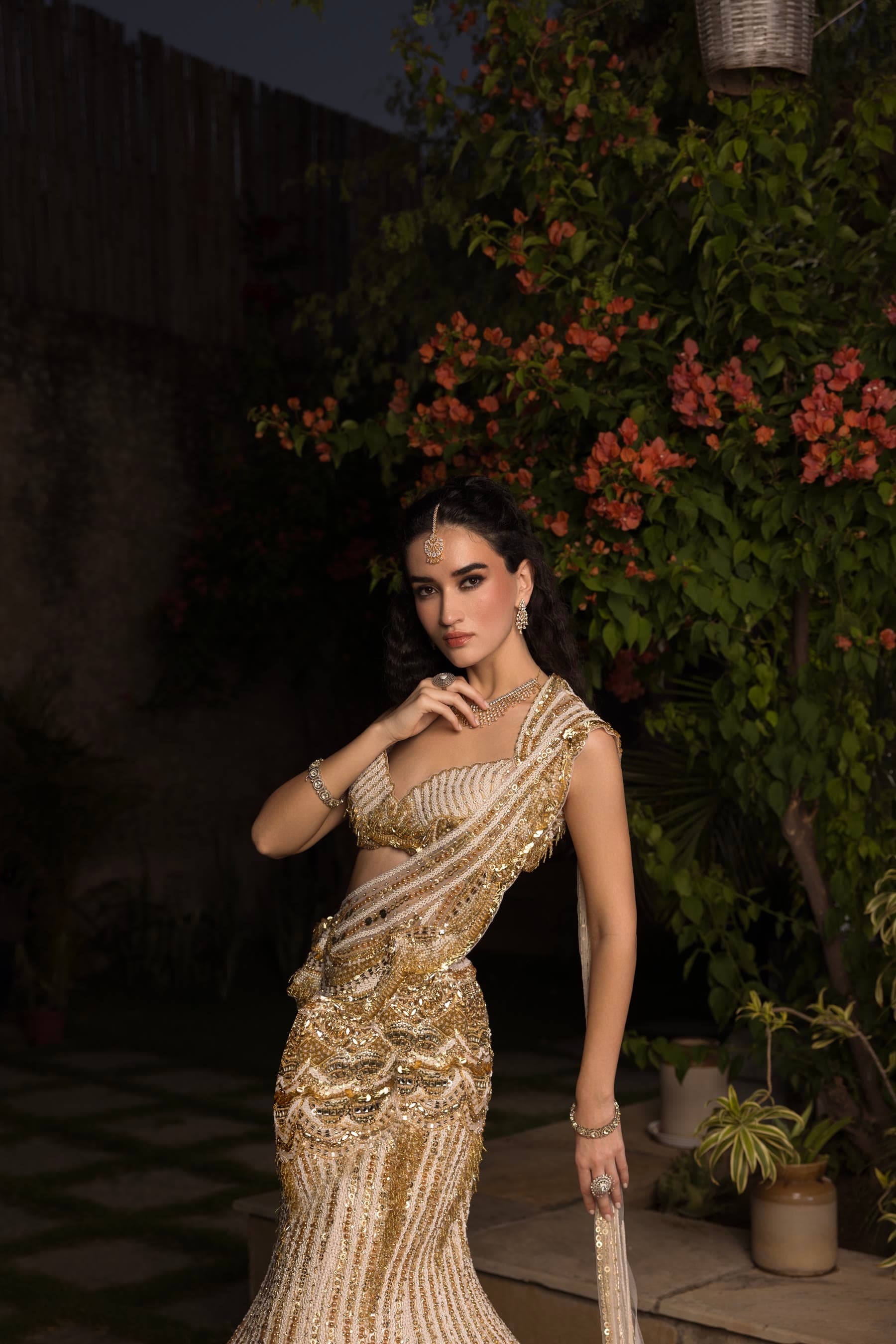 A bride in a gold sari, hand at her chin, after dark