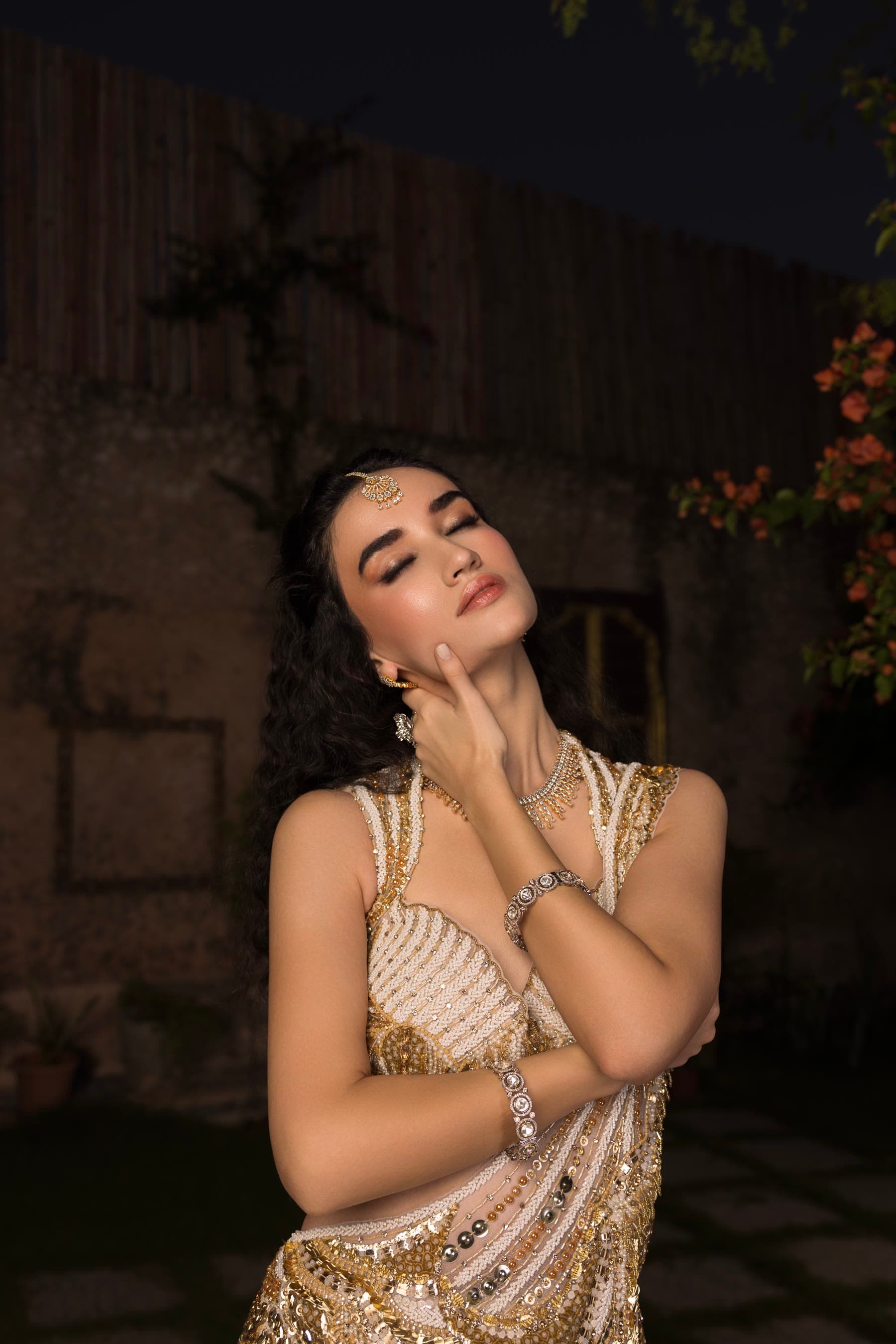 Hands lifted to the face, eyes closed, gold at the wrist